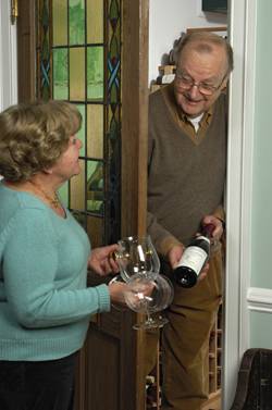 Rick Barry and Linda Cox select a wine from the extensive collection stored in their wine room. An antique door featuring a stained glass panel separates the wine room from the formal dining room.